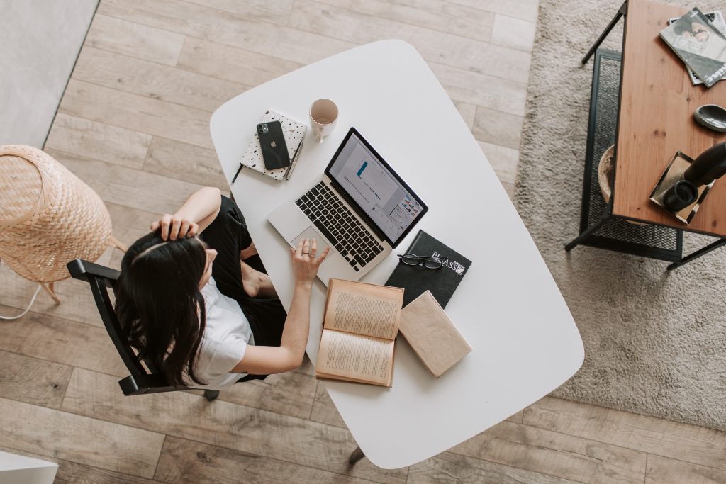 Somebody working at a desk on a laptop with various books and notebooks around them