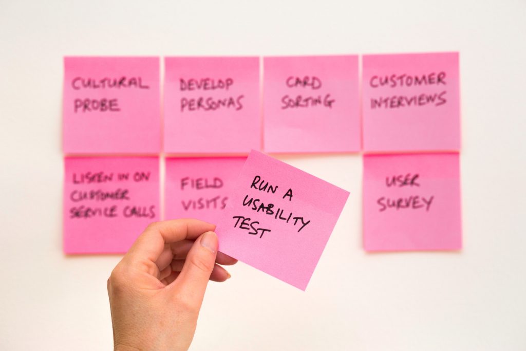 A selection of pink post-it notes, with somebody holding one on where 'RUN A USABILITY TEST' is written on it