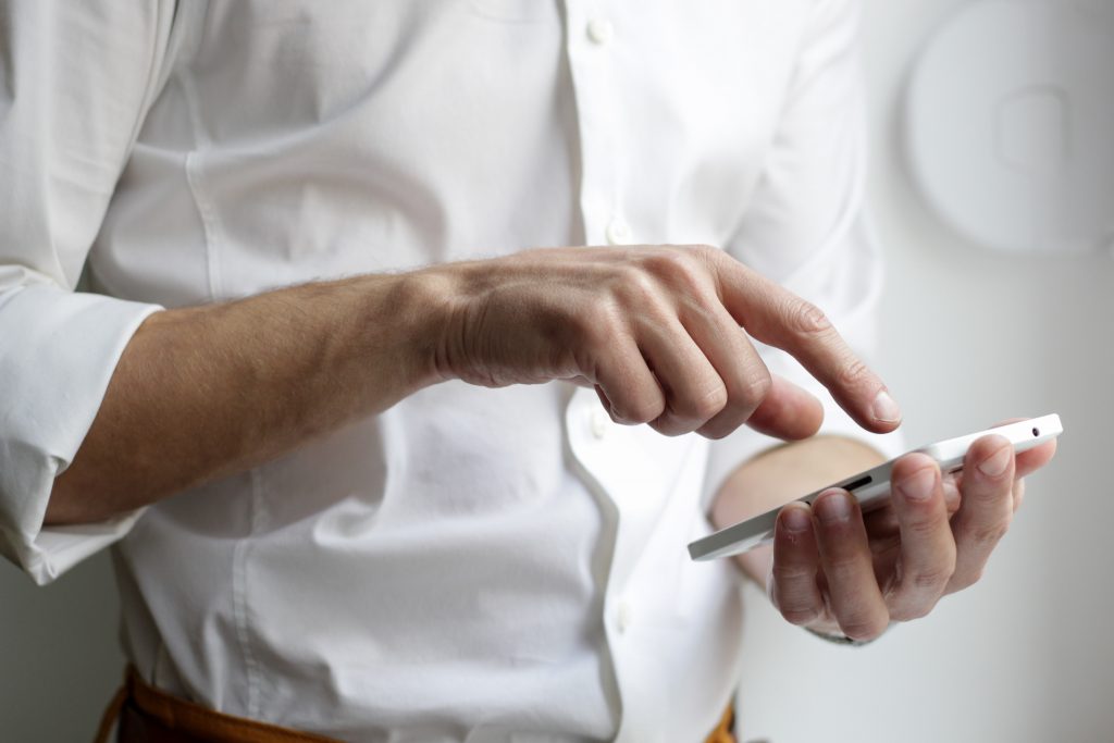 A person wearing a white shirt holding and point at a mobile phone