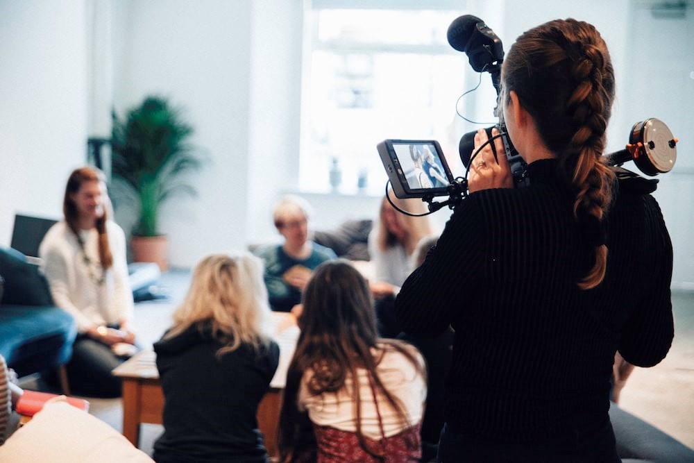 A videographer filming of a group of people gathered around a coffee table