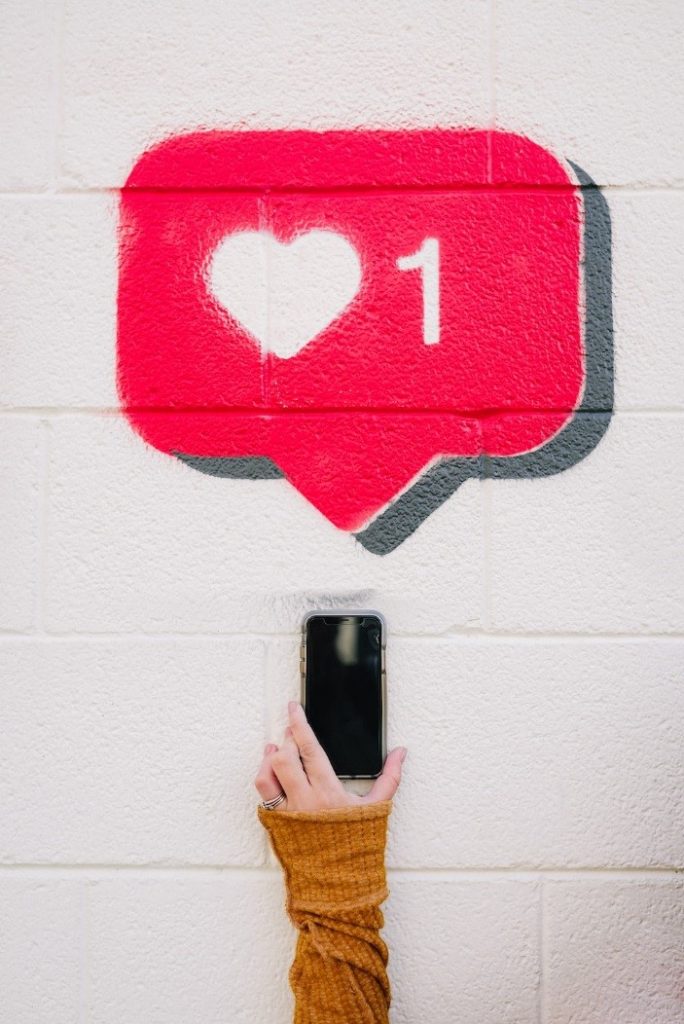 A social media 'like' icon in a red speech bubble painted on a wall with a phone held up to it